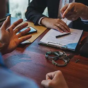 A lawyer consults with a client, with handcuffs on the table, illustrating criminal defense for a sex crime accusation.